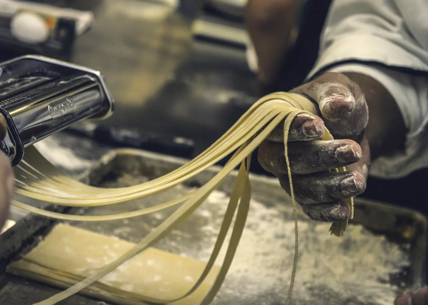 Hände ziehen frische Tagliatelle aus der Nudelmaschine