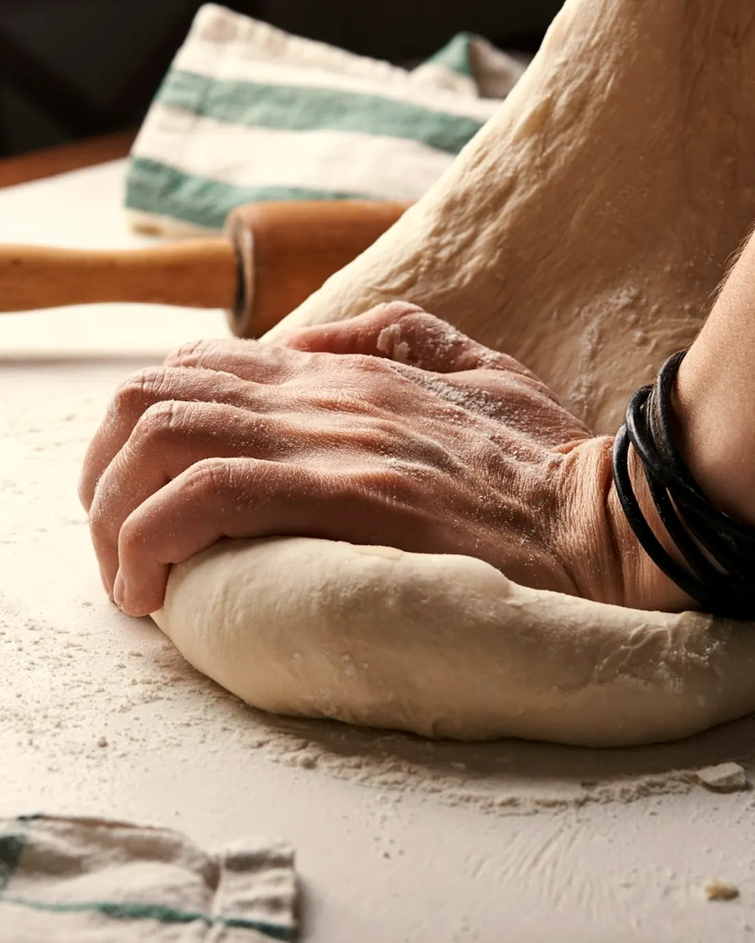Hände kneten Nudelteig auf einer bemehlten Arbeitsfläche